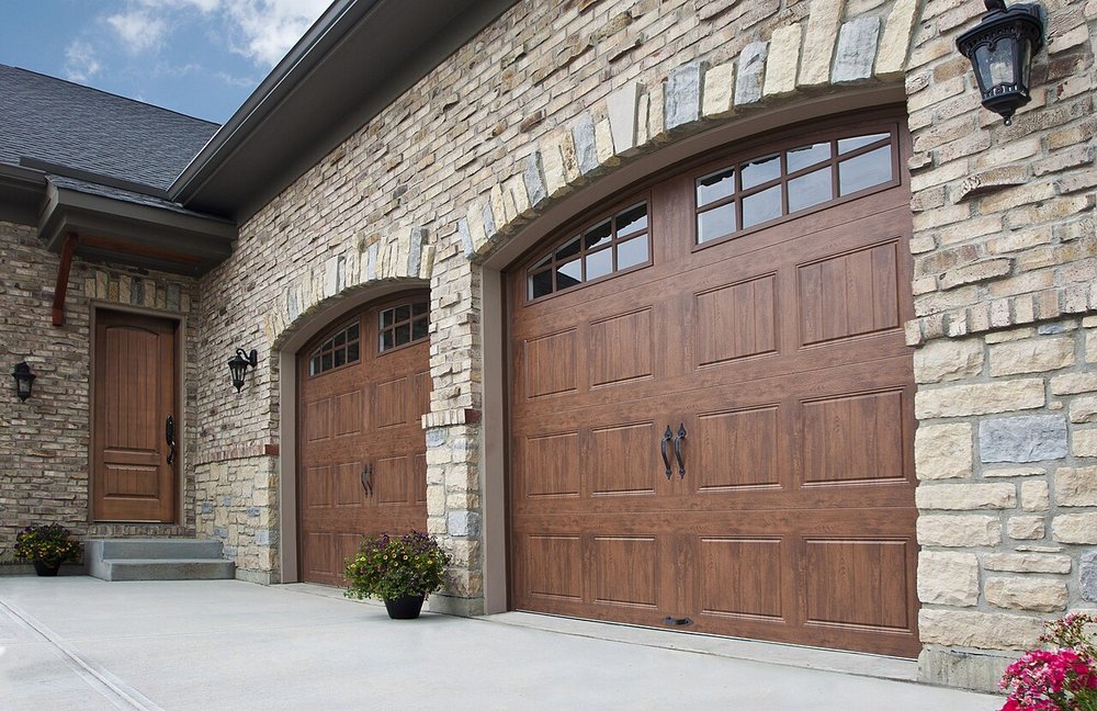 Arched wood-grain carriage-style garage doors set in a stone-clad house