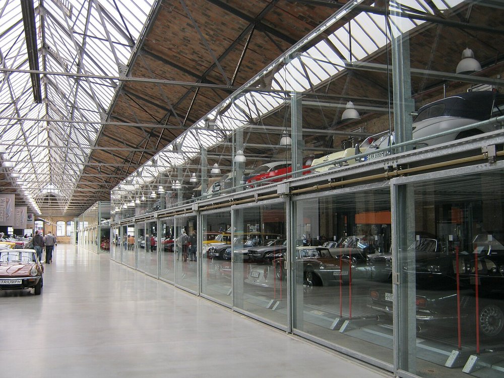 Collector cars stored in glass-fronted boxes along a skylit storage hall