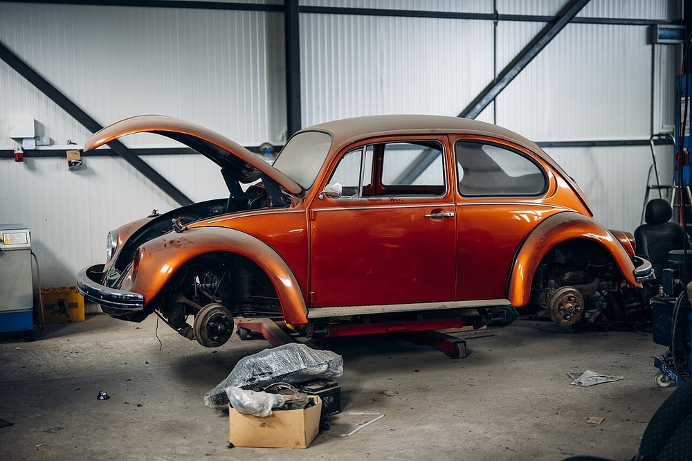 An orange classic Beetle under restoration in a well-lit garage workshop